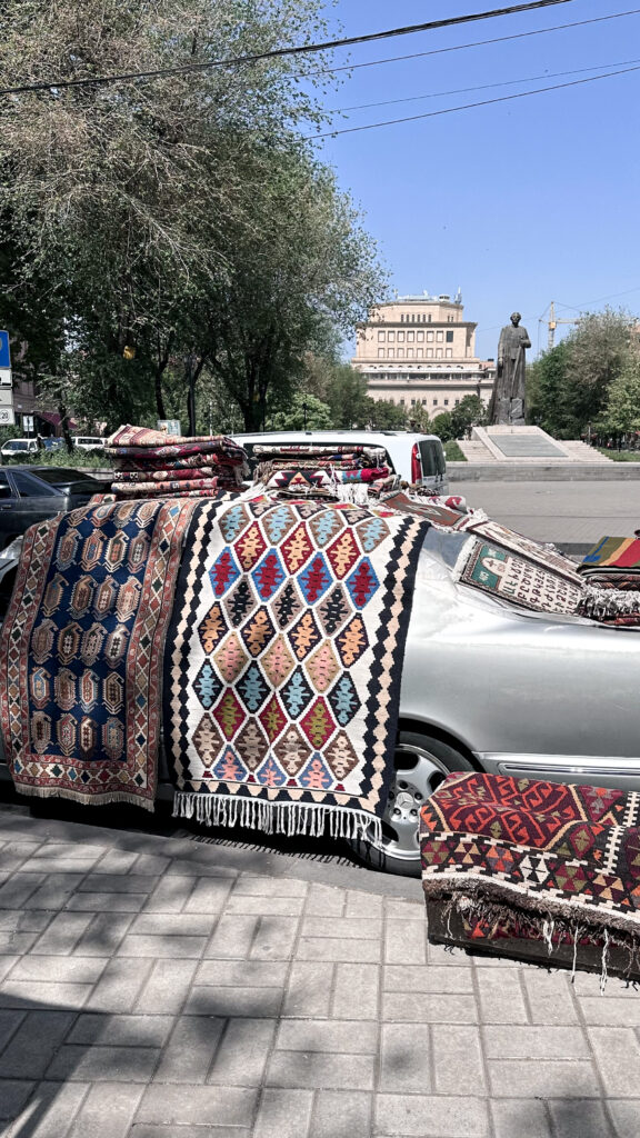 Venditore di tappeti alternativo con merce esposta sulla sua auto, al Vernissage di Yerevan
