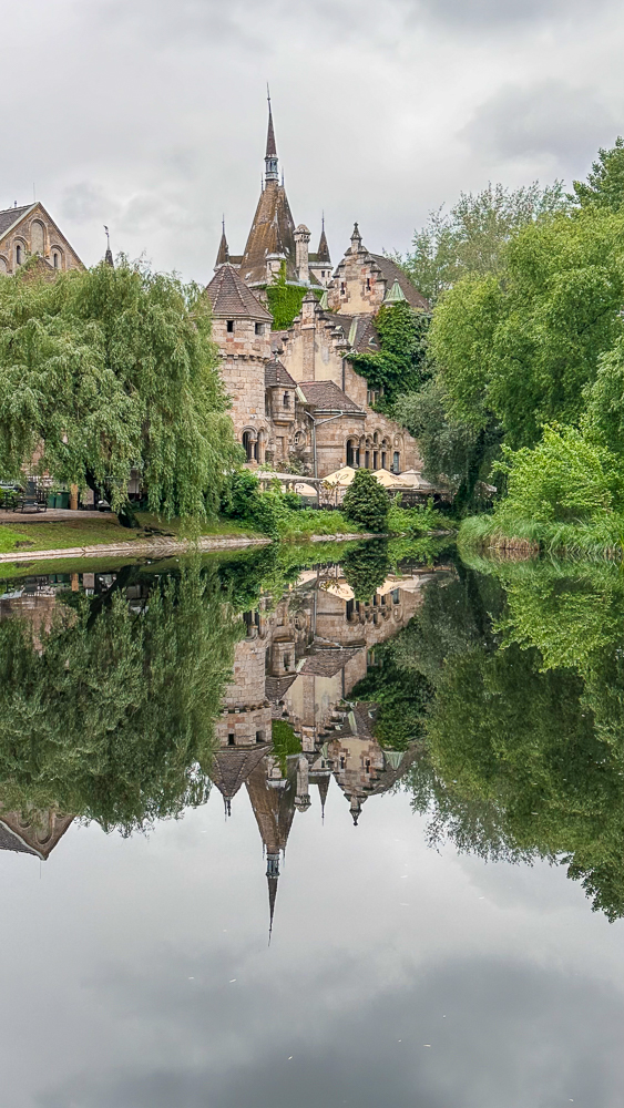 castello Vajdahunyad che si specchia nell'acqua circondato dal verde nel parco cittadino di budapest
