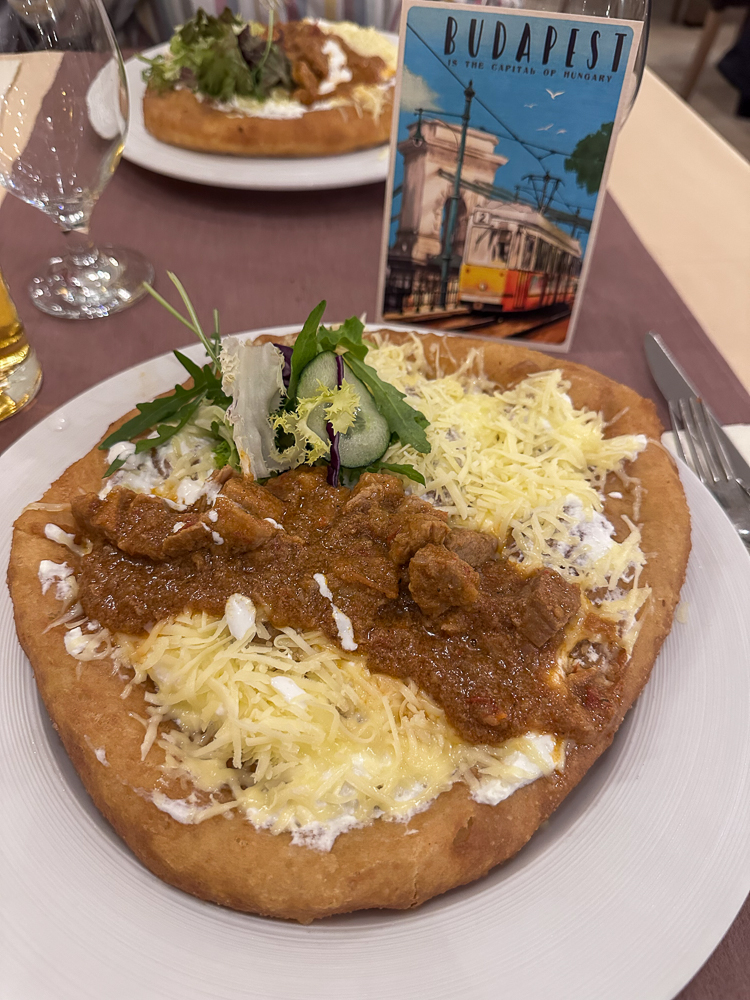 Langos, pizza fritta ungherese, condita con formaggio, panna acida e gulasch
